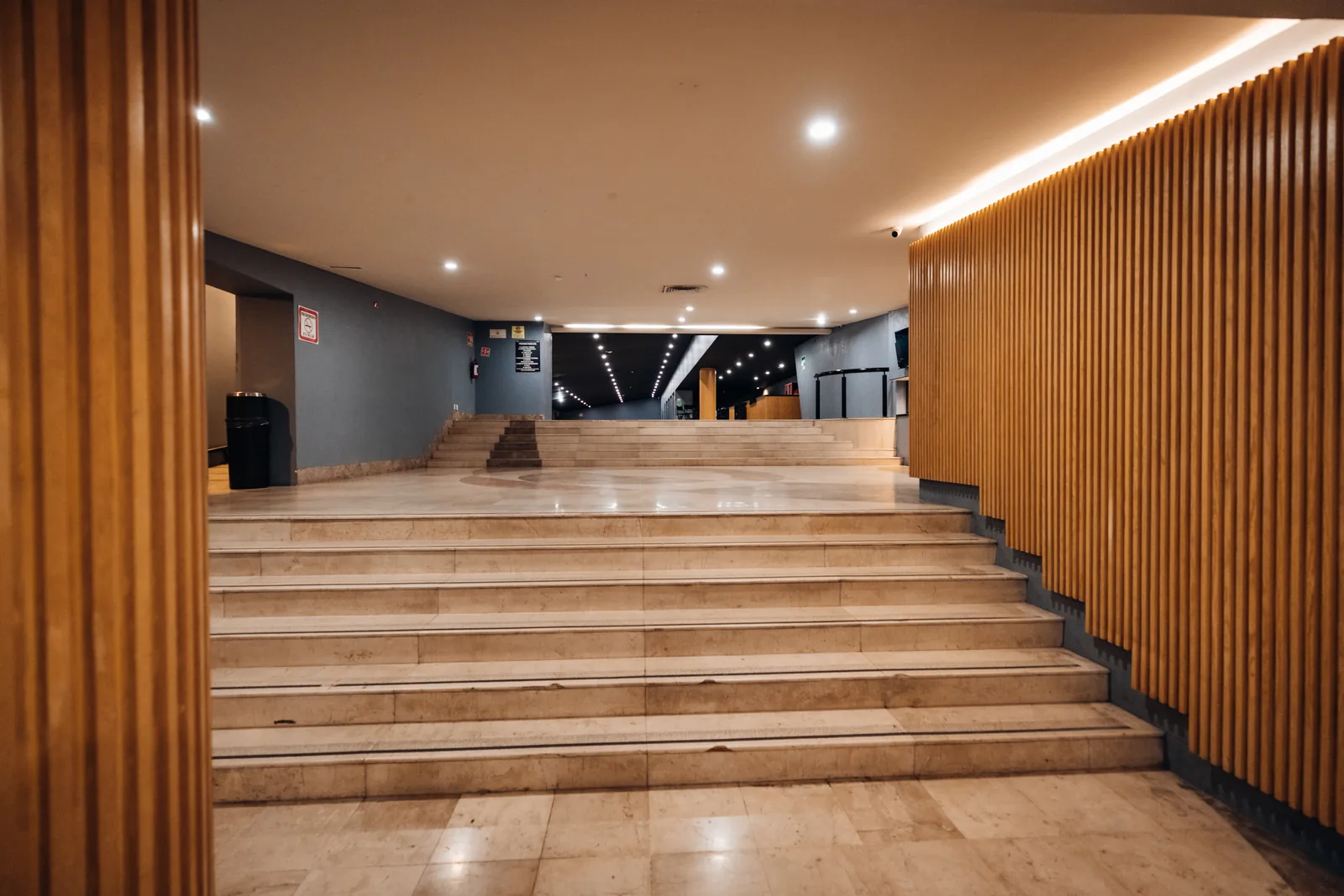 Interior de edificio con escaleras blancas y paredes de madera y gris iluminadas por luces en el techo.