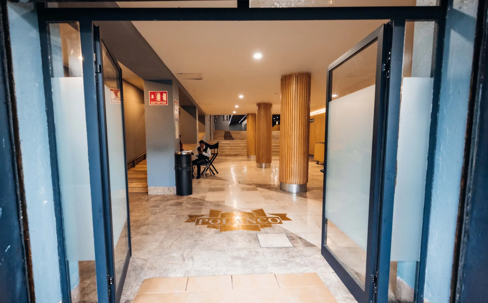Entrada abierta con columnas de madera y piso de mármol con logo de FORO POLANCO.