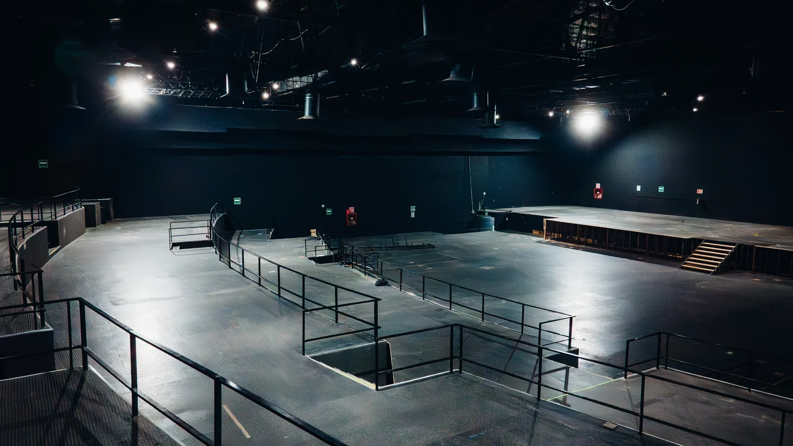 Interior de un auditorio o salón de eventos vacío con escenario y barandales metálicos.
