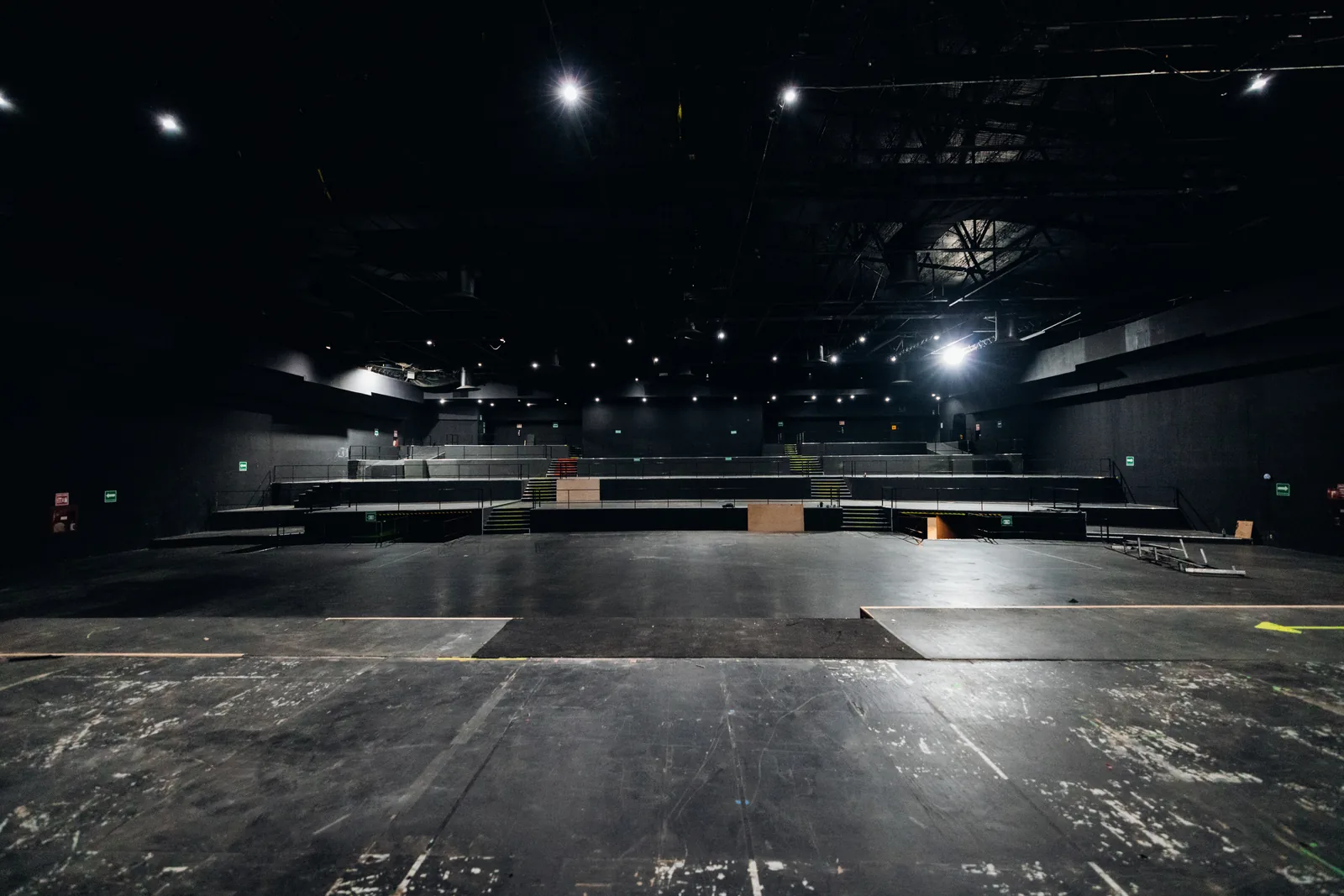 Escenario negro vacío con gradas escalonadas y luces en el techo oscuras en un auditorio.